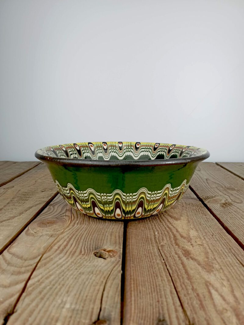 Obrazek przedstawia z boku: bułgarska gliniana zielona miska obiadowa - o średnicy ok. 20cm i pojemności ok. 0,95l, z wielokolorowym ludowym wzorem. Oryginalna ceramika bułgarska, produkt ręcznie wykonany i malowany.
