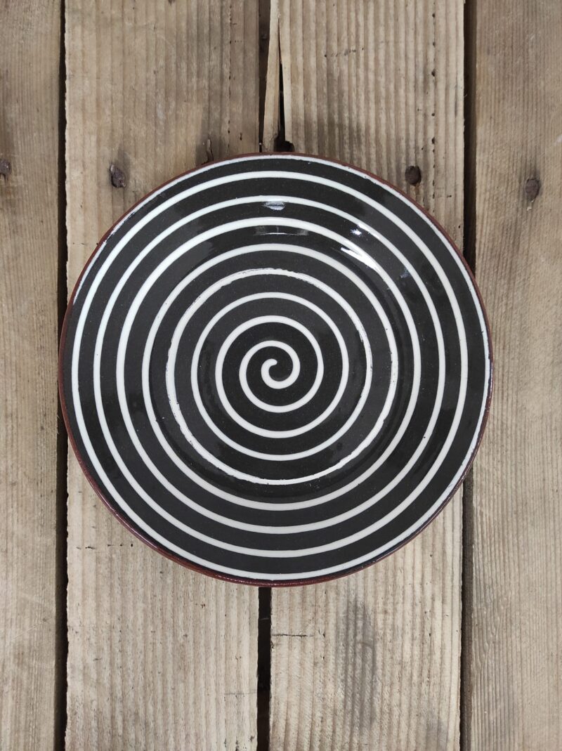 Obrazek przedstawia: bułgarski gliniany czarny talerzyk deserowy, z białym wzorem spirali, o średnicy ok. 18cm. Oryginalna ceramika bułgarska, talerz ręcznie wykonany i malowany.